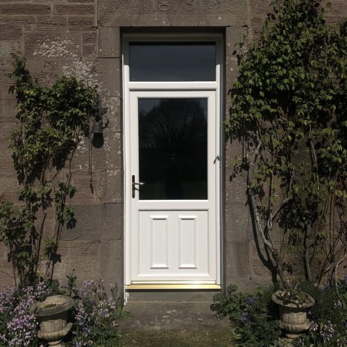 A white door with two windows and plants on the outside of it.